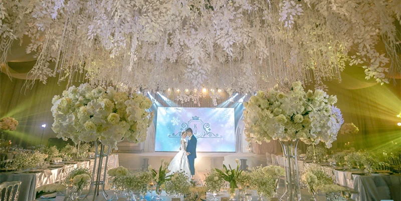Wedding ceremony setting with a central LED screen framed by white floral arrangements